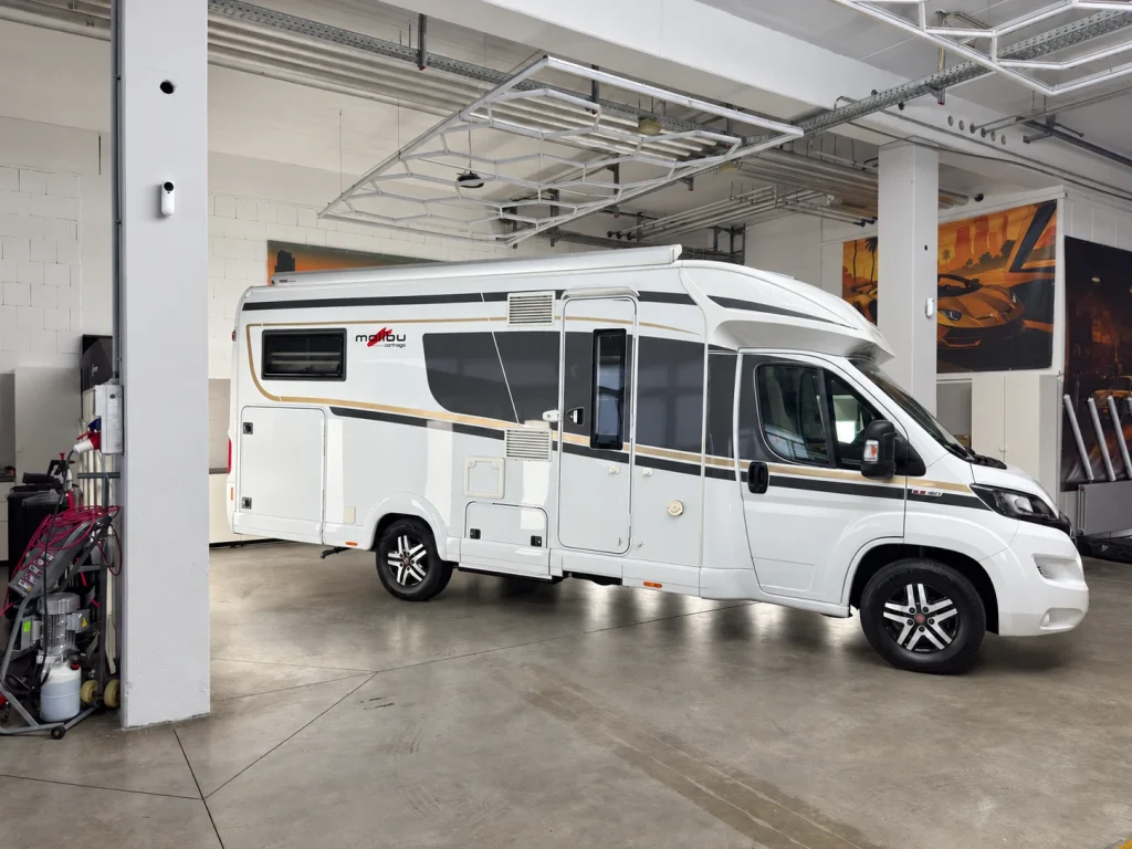 Weißes Wohnmobil in der Werkstatt von WrapIndustries, Seitenansicht; Kennzeichen unkenntlich.